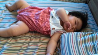 ベッドで指をしゃぶりお昼寝する赤ちゃん